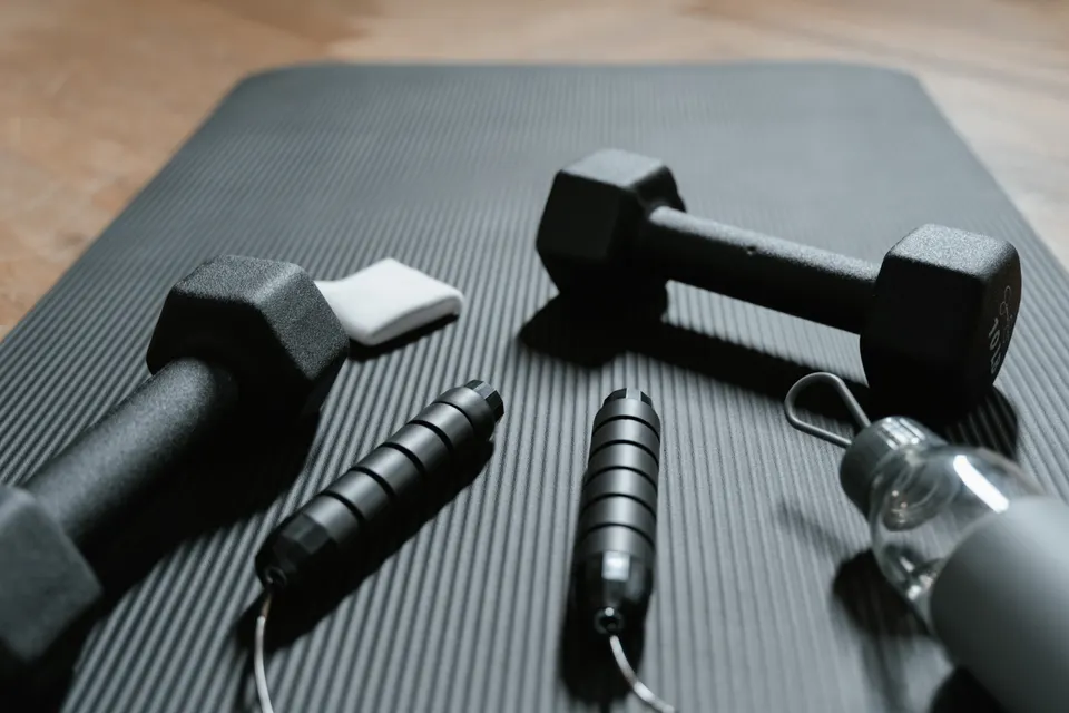 A yoga mat, dumbbells, skipping rope and water bottle ready for a home workout